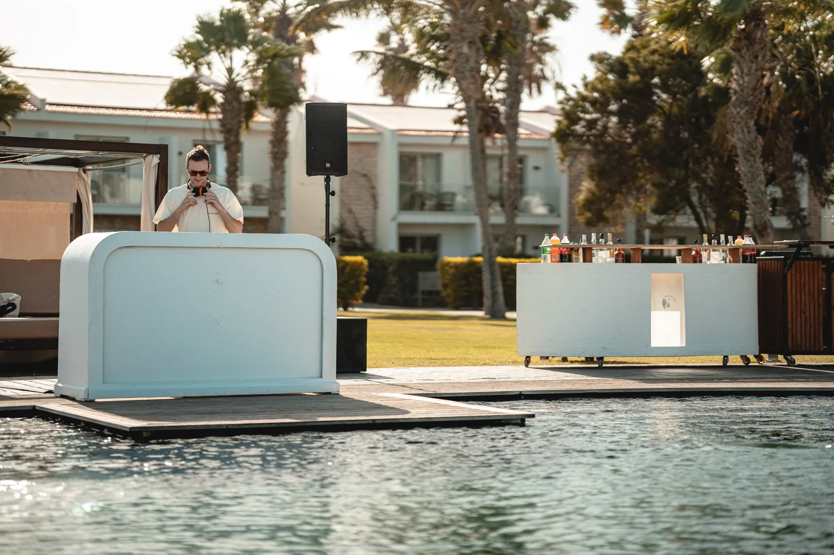 Weißes DJ-Pult auf einem Steg am Pool, dahinter Palmen und Strandhütten auf den Kapverden