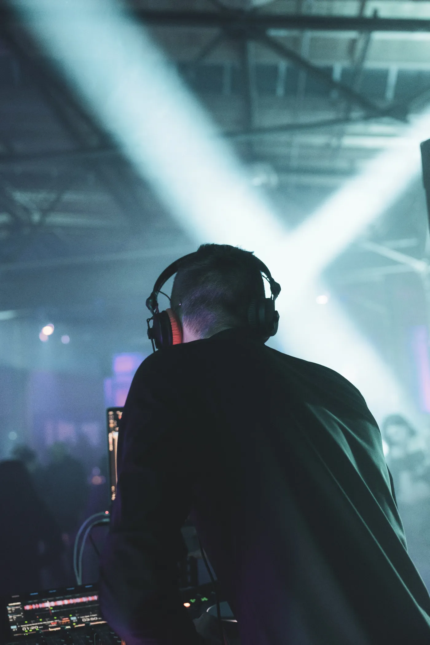 DJ Moritz mit Kopfhörern am Pult, über ihm kreuzen sich weiße Lichtkegel