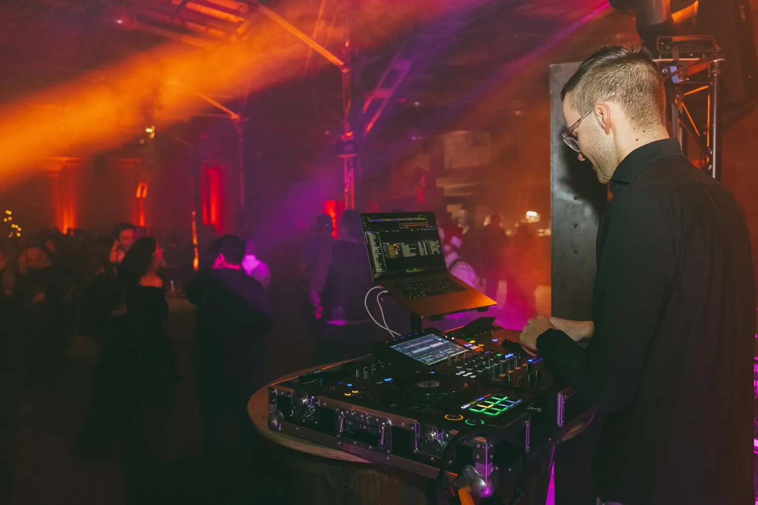 DJ Moritz am Pult bei einer Firmenfeier, dahinter die Tanzfläche im orangen Licht
