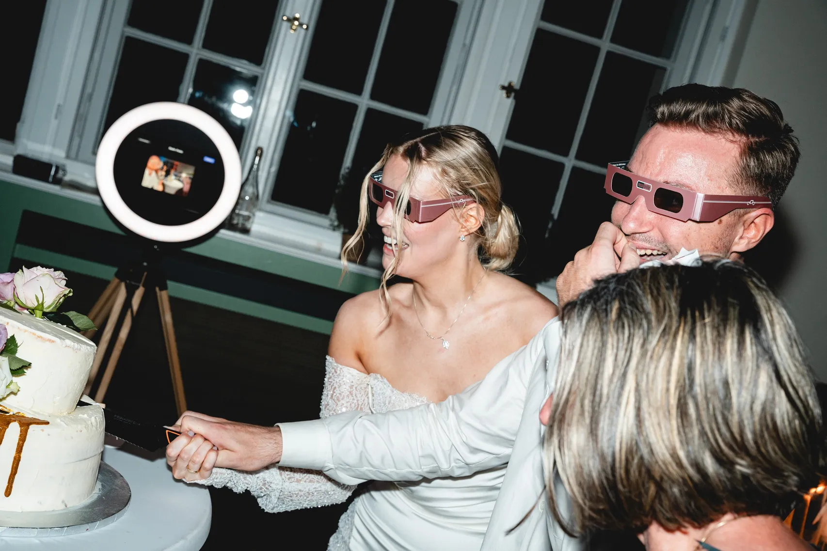 Brautpaar mit Partybrillen vor der Fotobox mit Ringlicht, daneben die Hochzeitstorte