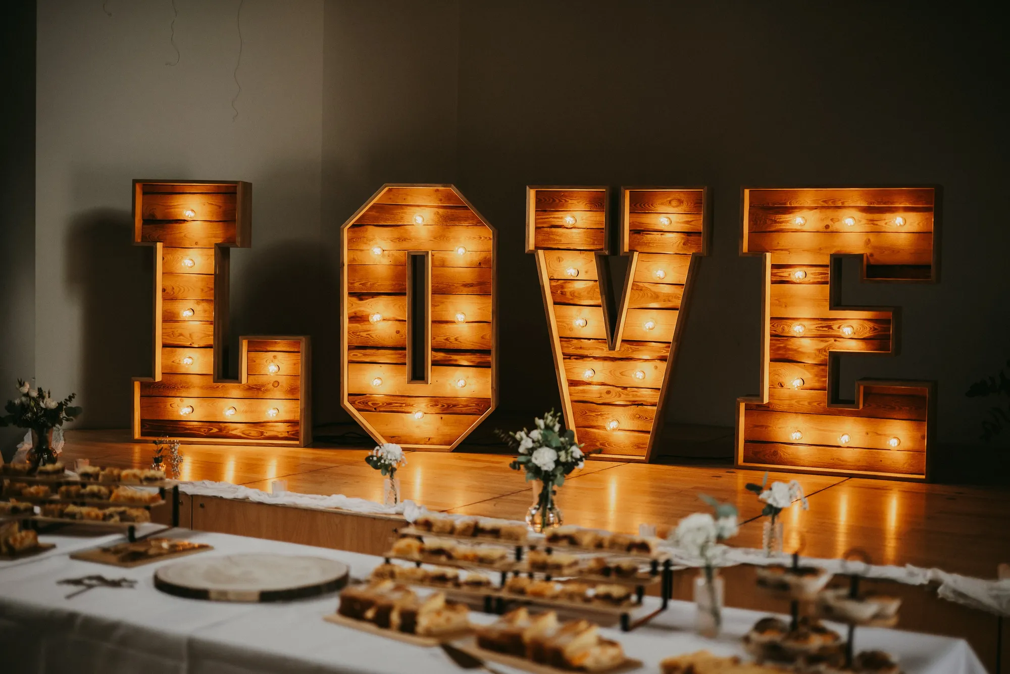 Hochzeitstafel mit weißen Tischdecken und leuchtenden LOVE-Buchstaben im Hintergrund